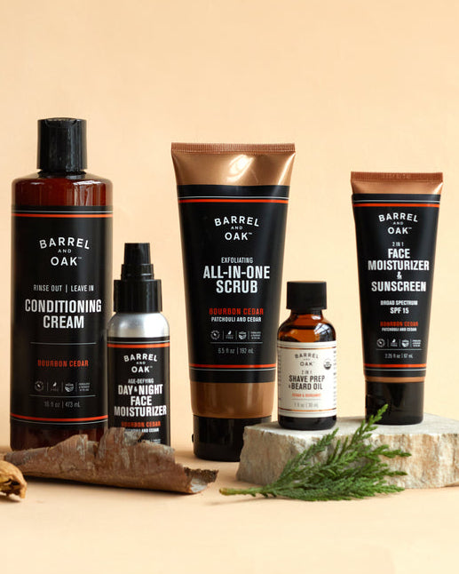 The SPF 15 Moisturizer - Bourbon Cedar (2.25 fl oz.) is shown on a beige surface, styled with wood and greenery details.