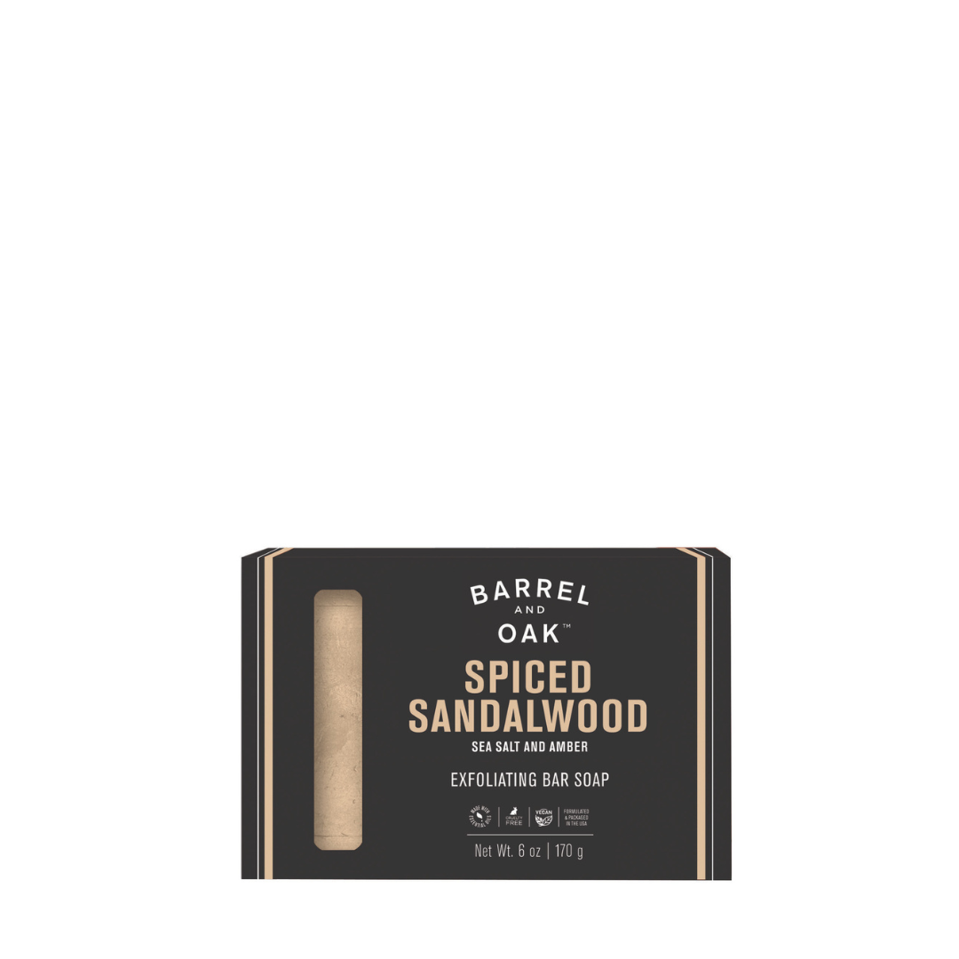 Exfoliating Soap Bar - Spiced Sandalwood 6 oz features sustainable palm oil, sea salt, amber, and kaolin clay. The sleek black packaging includes a label highlighting key ingredients and a window displaying the bar inside.