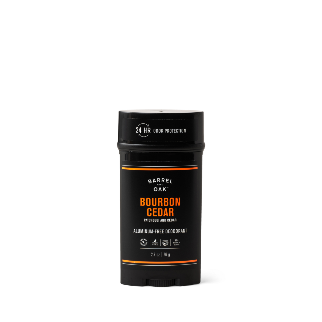 A black stick of Aluminum Free Deodorant - Bourbon Cedar 2.7 oz. with orange and white text, offering essential oils for 24-hour odor protection. The cruelty-free container sits on a white background and weighs 2.7 oz (76 g).