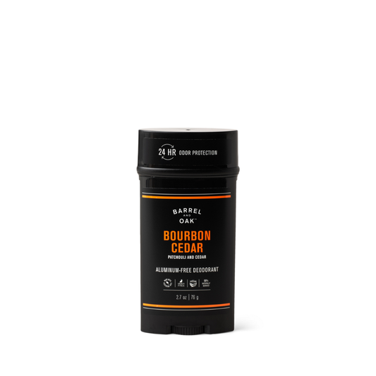 A black stick of Aluminum Free Deodorant - Bourbon Cedar 2.7 oz. with orange and white text, offering essential oils for 24-hour odor protection. The cruelty-free container sits on a white background and weighs 2.7 oz (76 g).