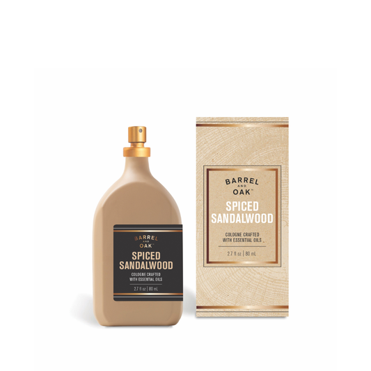 A beige bottle of Natural Fragrance Cologne - Spiced Sandalwood 2.7 fl oz. with a black label stands beside its matching box, showcasing its refined bergamot cedar scent and sophisticated design.