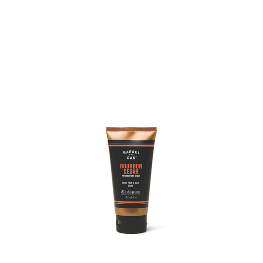 A 2.5 fl oz tube of Barrel & Oak Hair, Face, and Body All In One Wash - Bourbon Cedar is centered on a white background. The black tube with copper accents displays white and orange text for an all-in-one men's wash.
