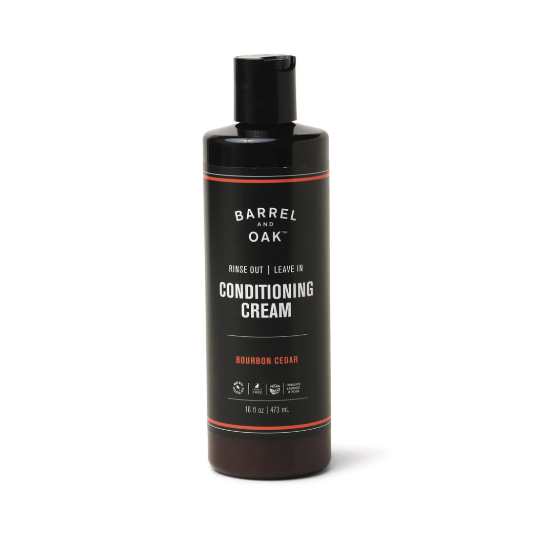 A 16 oz black bottle of Rinse Out/Leave In Conditioning Cream - Bourbon Cedar, enriched with organic olive oil for healthy hair growth. It features a flip-top cap and is scented with Bourbon Cedar.