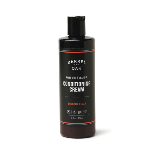 A 16 oz black bottle of Rinse Out/Leave In Conditioning Cream - Bourbon Cedar, enriched with organic olive oil for healthy hair growth. It features a flip-top cap and is scented with Bourbon Cedar.