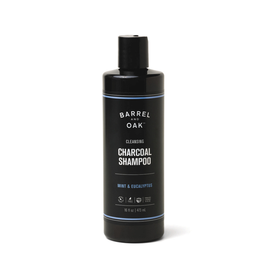 A black bottle of Cleansing Charcoal Shampoo - Mint & Eucalyptus 16 oz, featuring white text and a blue accent, is perfect for scalp detox and hair refreshment with this organic cleanser.