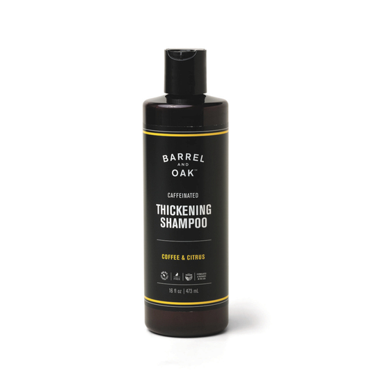 A black bottle of Caffeinated Thickening Shampoo - Coffee & Citrus 16 oz stands upright on a white background, featuring white and gold text. This biotin shampoo helps promote thicker-looking hair.