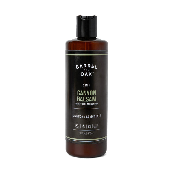 A black bottle of 2 in 1 Shampoo - Canyon Balsam with a minimalist label, flip-top cap, and containing desert sage, juniper, and organic shea butter. The bottle holds 16 fl oz (473 mL).
