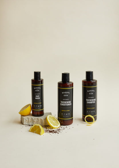Three bottles of Barrel Oak grooming products, including the Caffeinated Thickening Conditioner - Coffee & Citrus 16 oz., are displayed with lemon slices, coffee grounds, and a stone for healthier, thicker-looking hair.