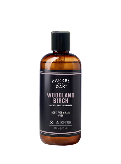 A 16 fl oz (473 ml) brown bottle of Hair, Face, and Body All In One Wash - Woodland Birch with a black label and cap. The label notes a spiced citrus and leather scent.