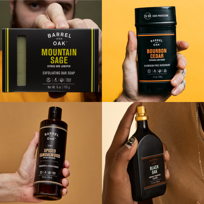 Four Barrel and Oak grooming products held by hands: Mountain Sage exfoliating bar soap, Bourbon Cedar aluminum-free deodorant, Spiced Sandalwood 2-in-1 shampoo & conditioner, and Black Oak cologne.